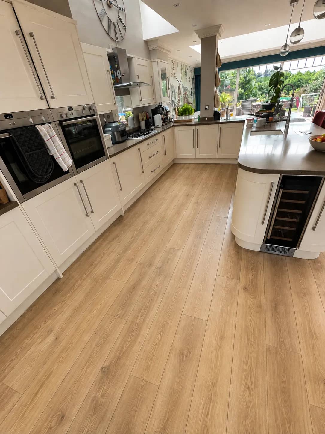 An open-plan kitchen with built-in ovens and a wood-effect floor left clean.