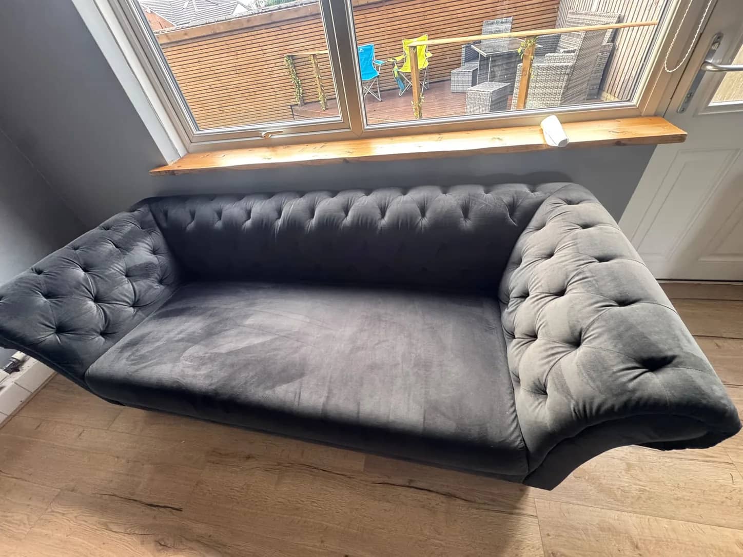 A grey velvet chesterfield sofa cleaned and left to dry beside a window.