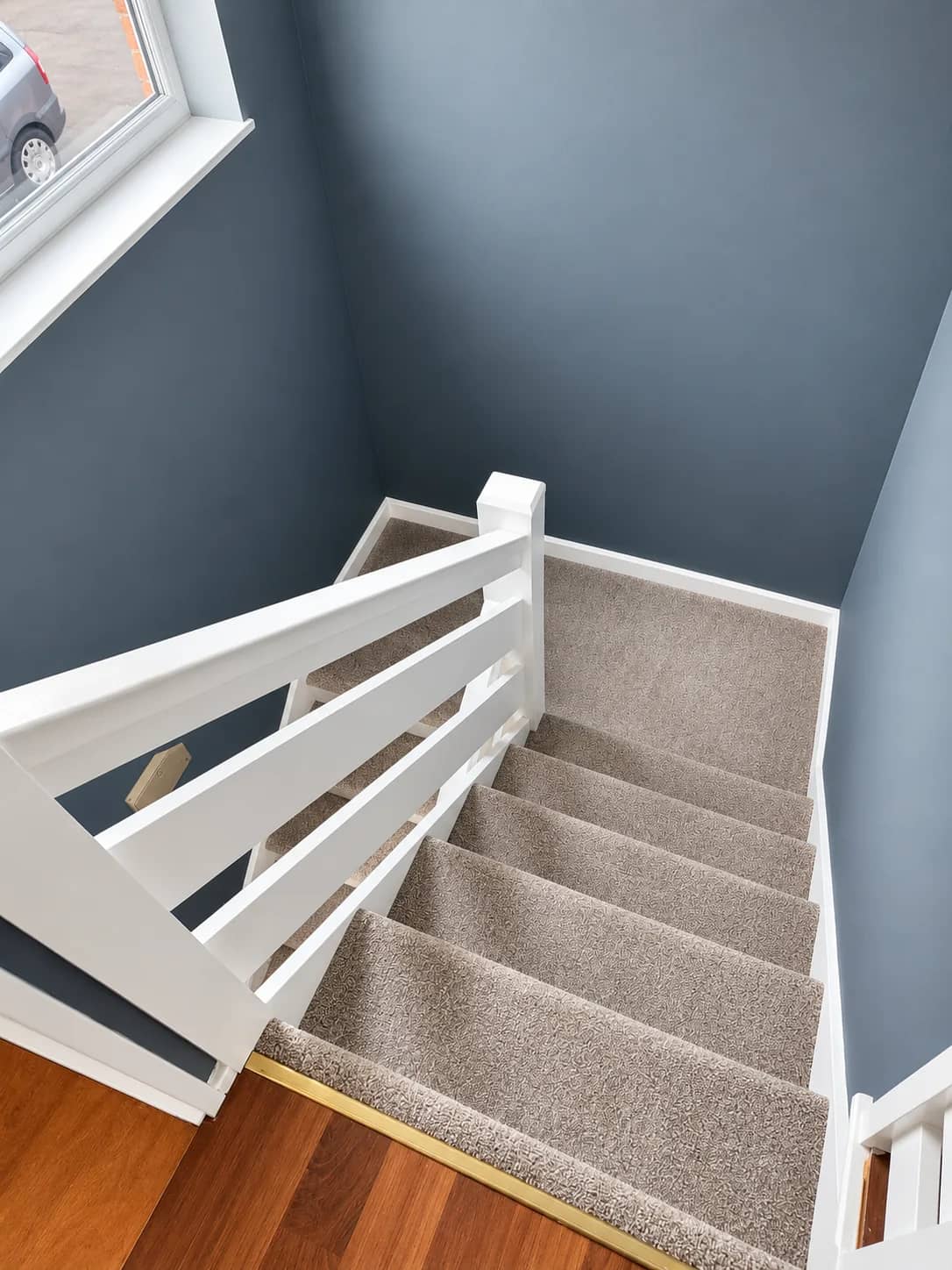 A stair carpet left clean beside white spindles.